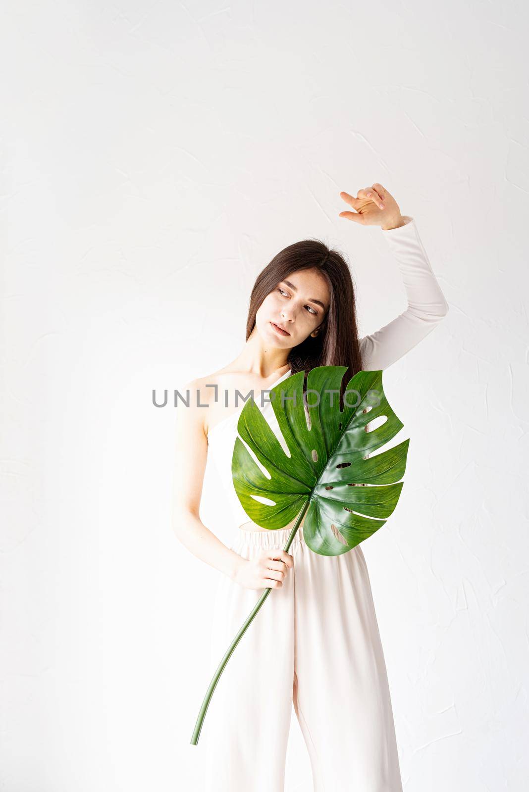Happy beautiful woman in cozy clothes holding a green monstera leaf by Desperada