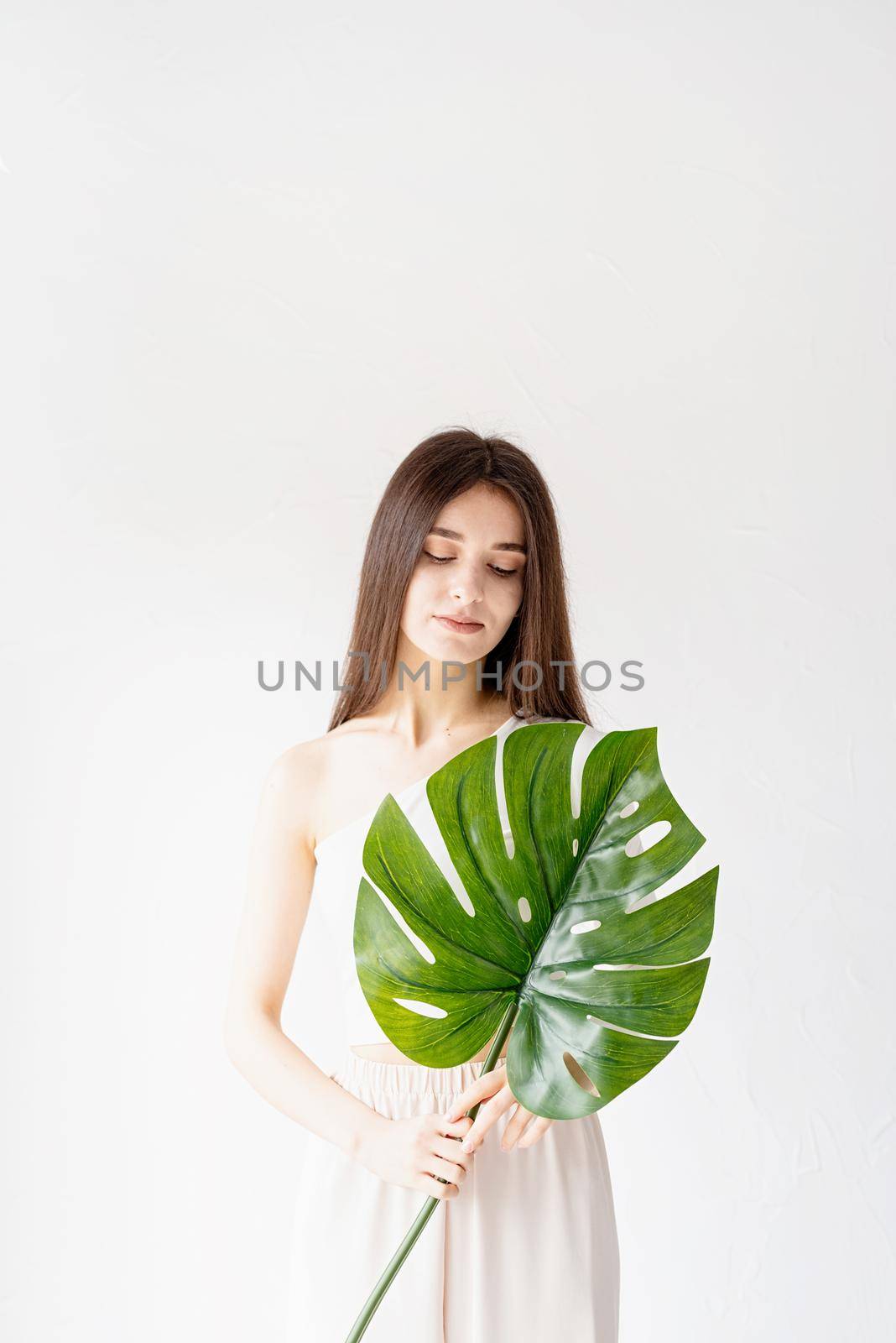 Happy beautiful woman in cozy clothes holding a green monstera leaf by Desperada