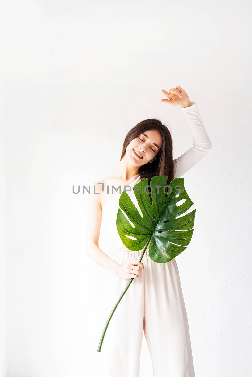 Spa and beauty. Self care and skin care. Happy beautiful woman in cozy clothes holding a green monstera leaf