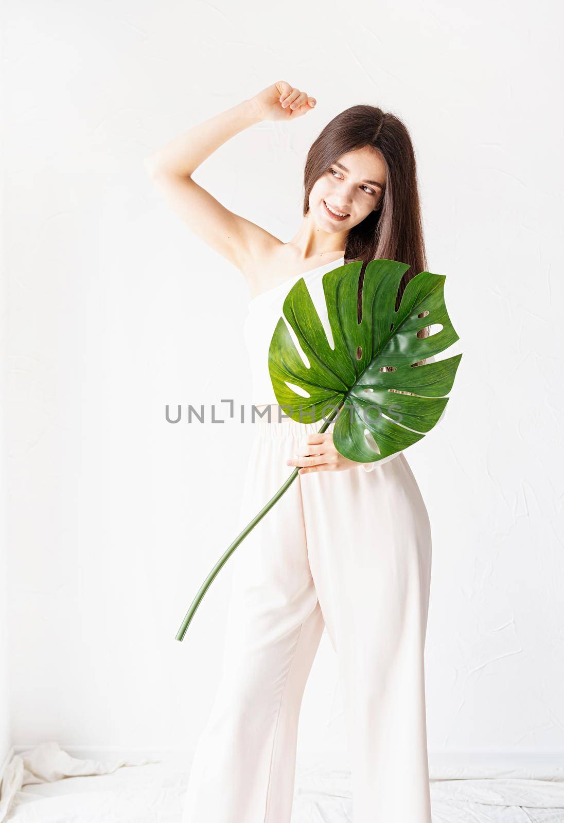 Spa and beauty. Self care and skin care. Happy beautiful woman in cozy clothes holding a green monstera leaf