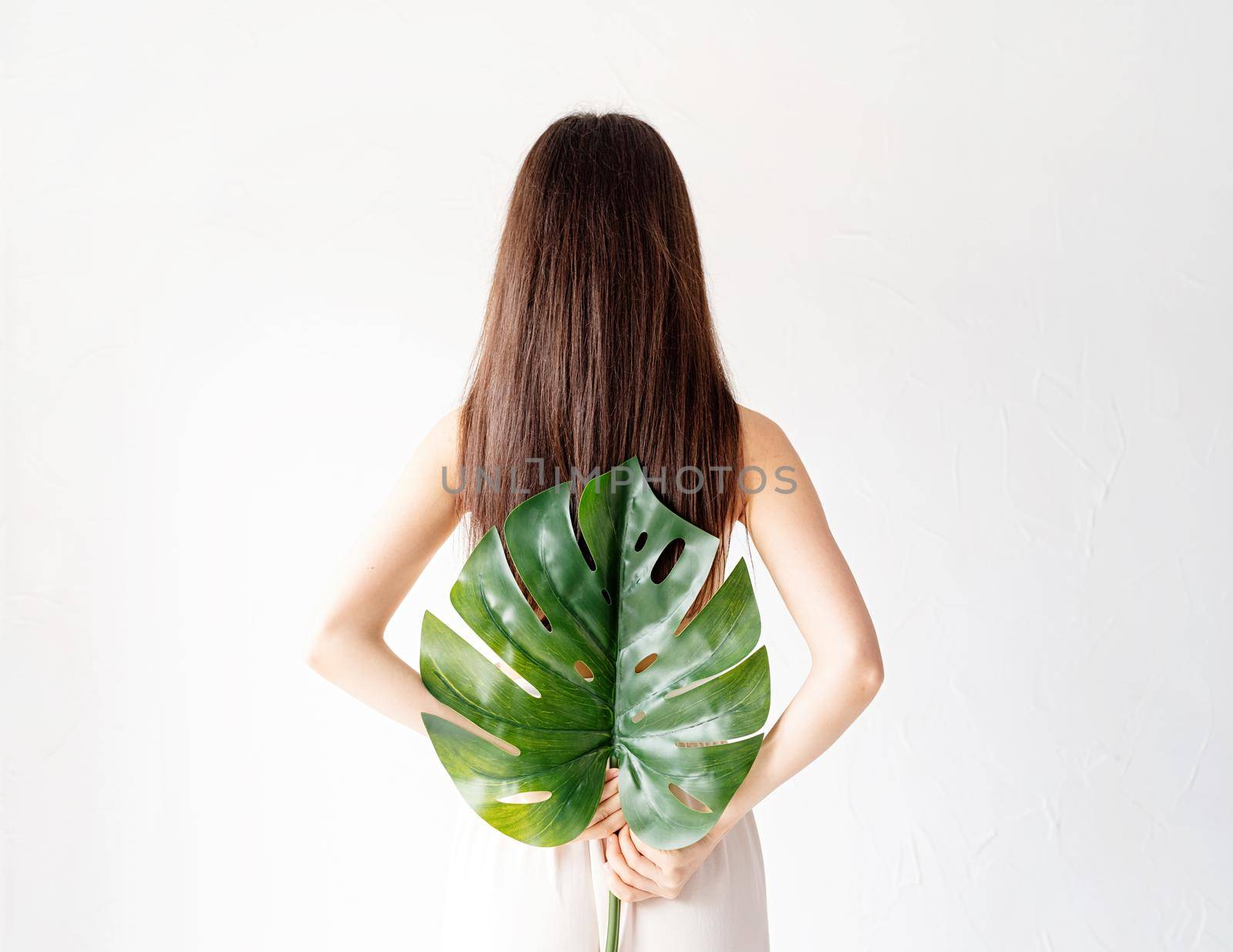 Spa and beauty. Self care and skin care. Happy beautiful woman in cozy clothes holding a green monstera leaf, rear view