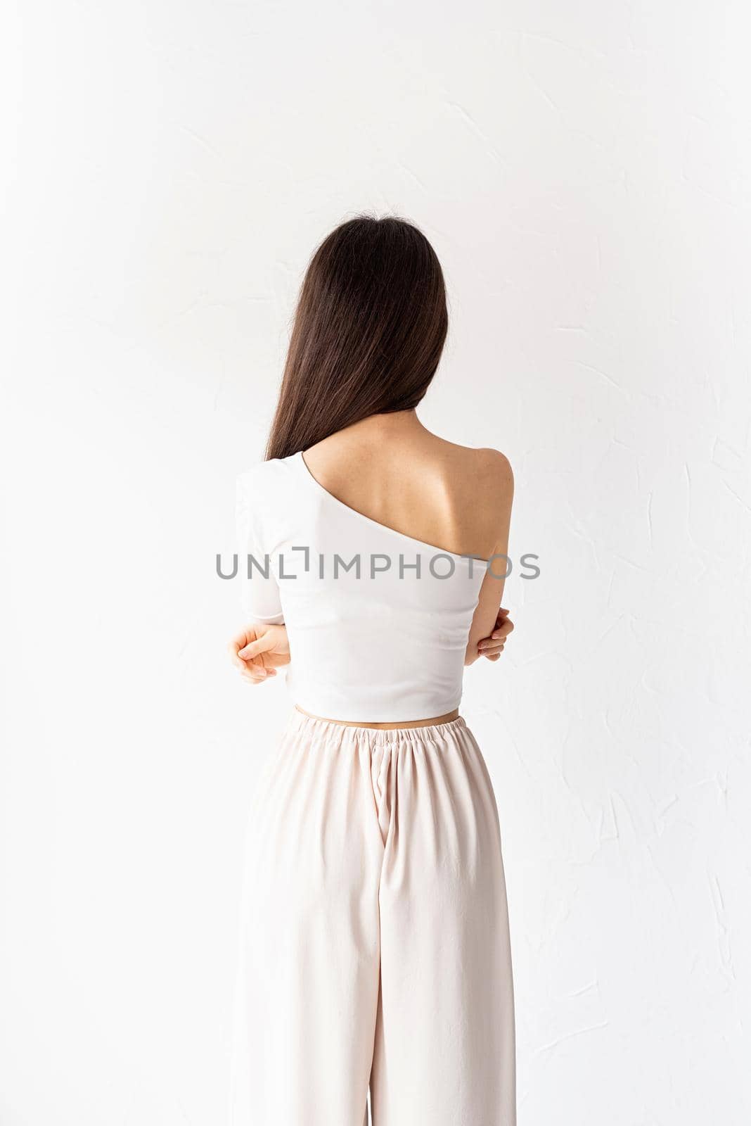 beautiful young woman with long hair in white cozy clothes on white background, view from behind by Desperada