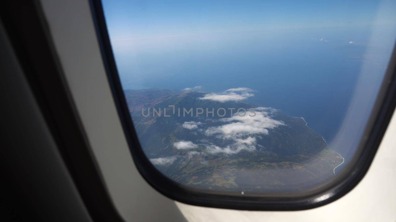aircraft porthole window with blue sea or ocean in it and small tropical islands. Looking through window aircraft during flight