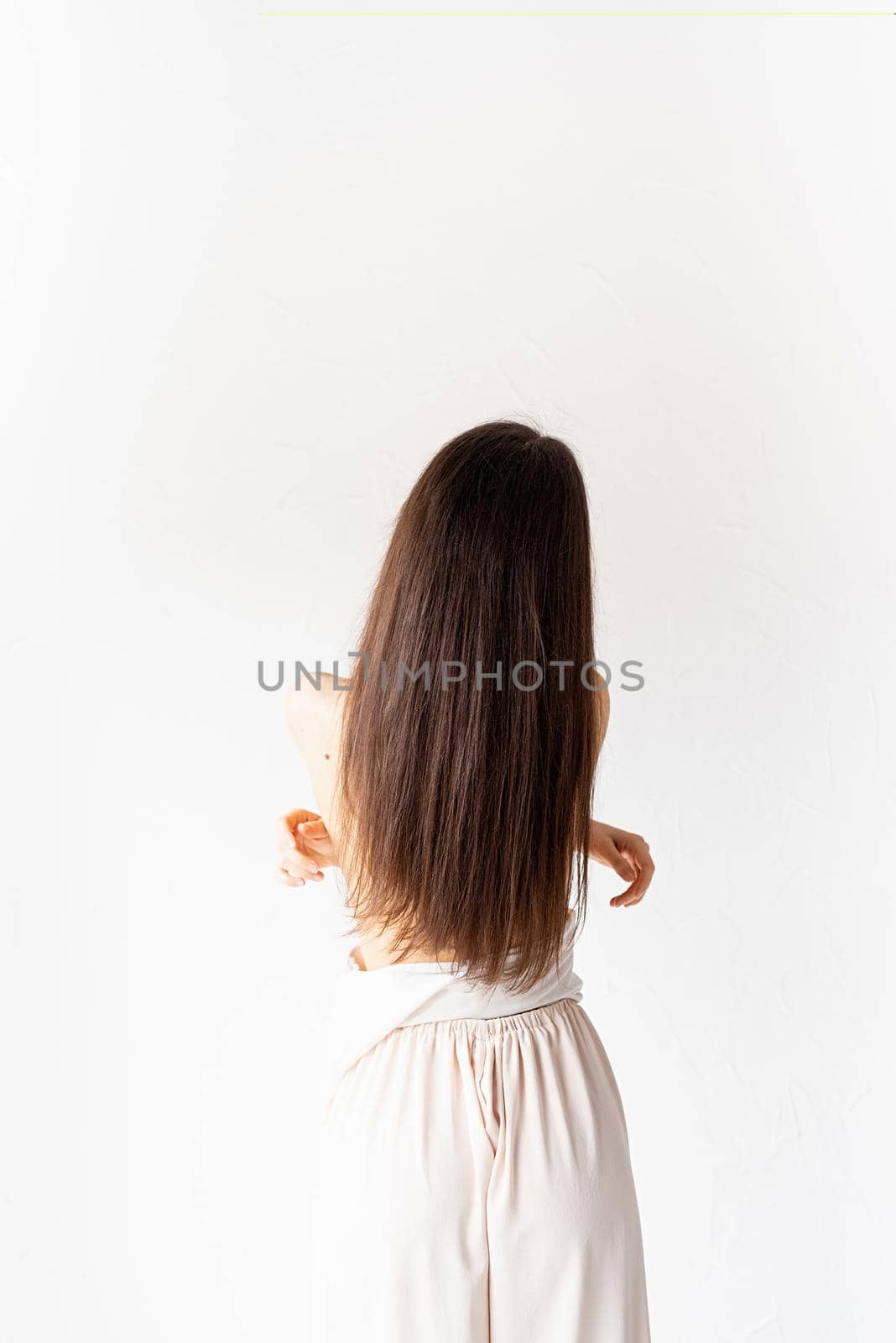Light and airy. beautiful young woman with long hair in white cozy clothes on white background, view from behind