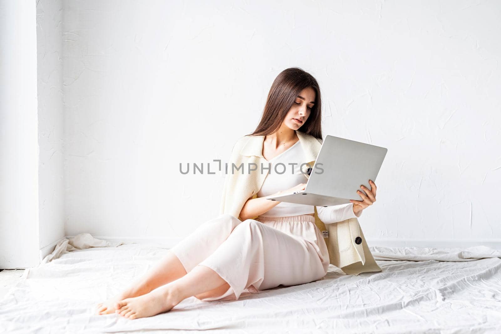 Beautiful young woman sitting on the floor and doing freelance project on laptop by Desperada