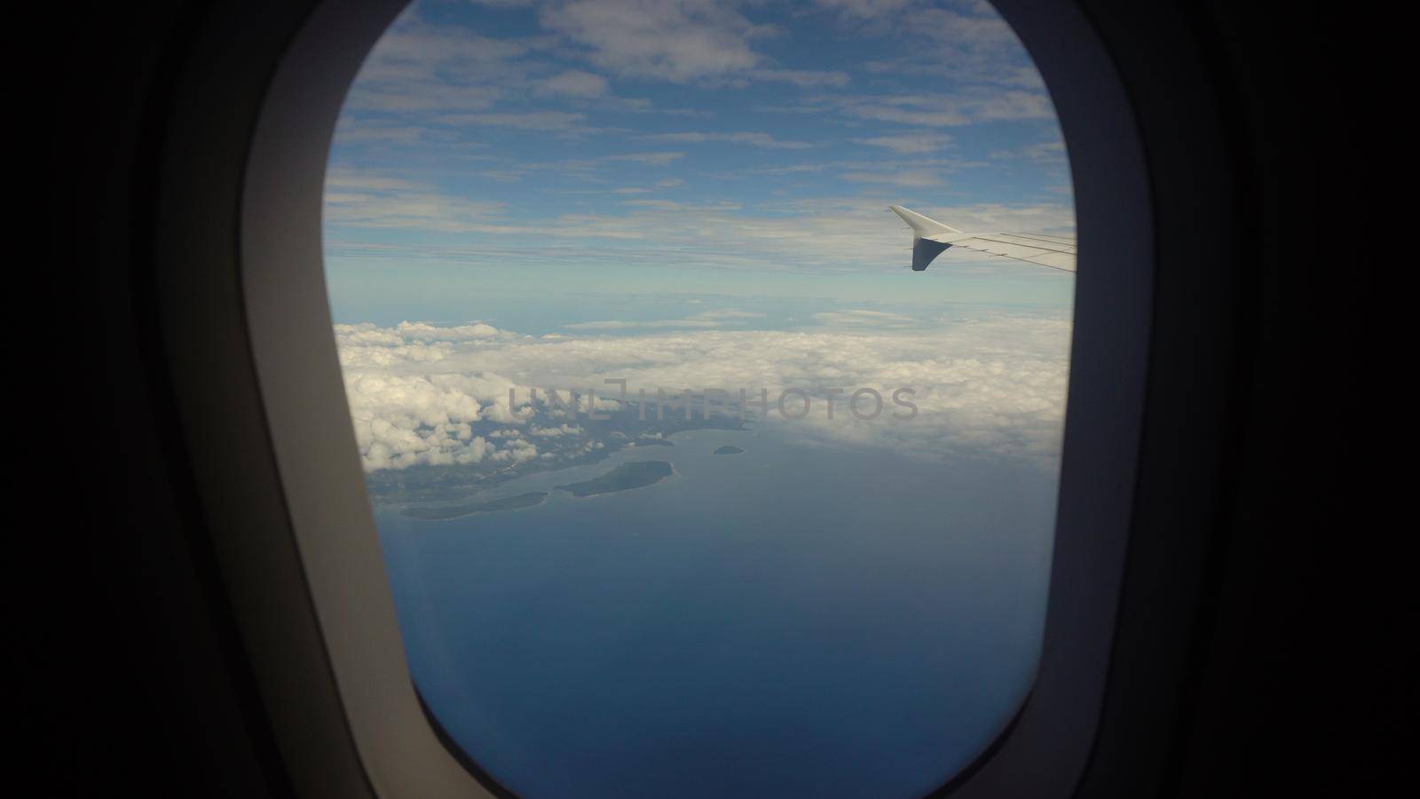 Airplane flying over blue sea and tropical island. Airplane wing through the porthole. Looking through window aircraft during flight