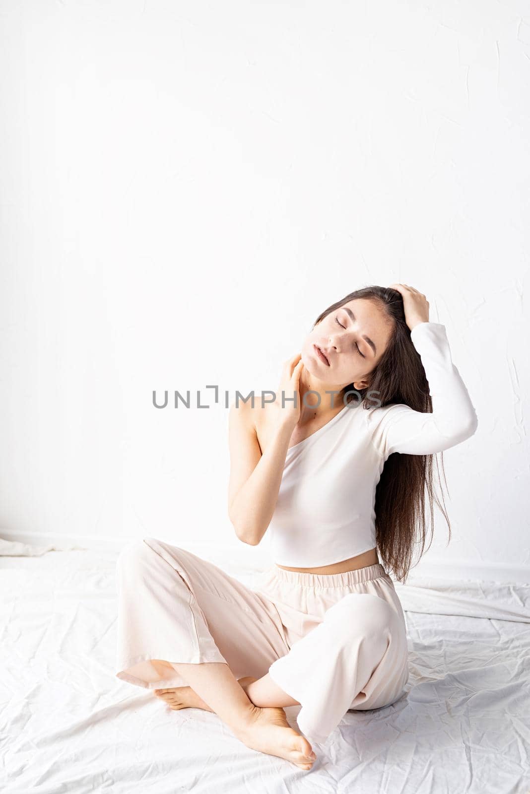 Light and airy. Portrait of beautiful woman in white cozy clothes sitting on the floor looking away