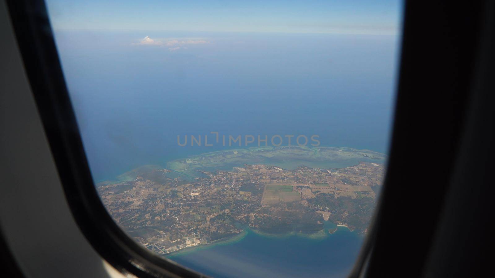 View through an airplane window on the tropical island, ocean, sky and clouds. Aerial view sea, clouds and sky as seen through window of an aircraft. Travel concept.