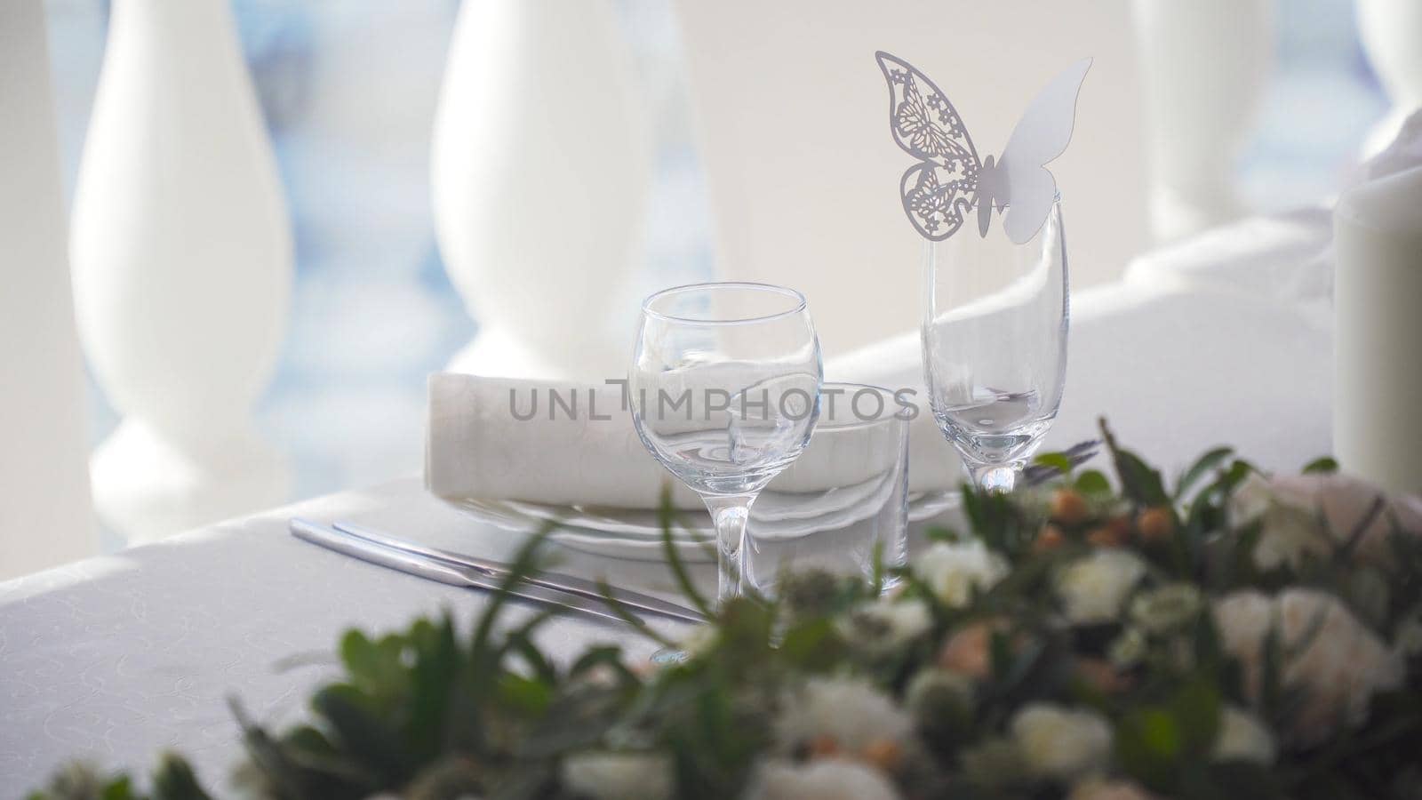 Banquet decorated table, with cutlery. Paper butterfly application on a glass. Wedding decor in the banquet hall. Serving of a festive table, plate, napkin, knife, fork. Table setting decoration. Romantic Dinner or other events.