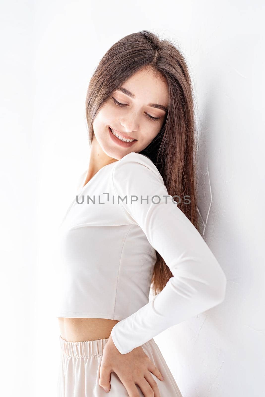 Close up of happy girl in white pajamas standing by the wall at home smiling