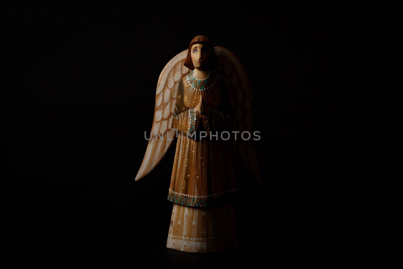 Wooden angel praying with half face in the dark against black background with copy space. High quality photo