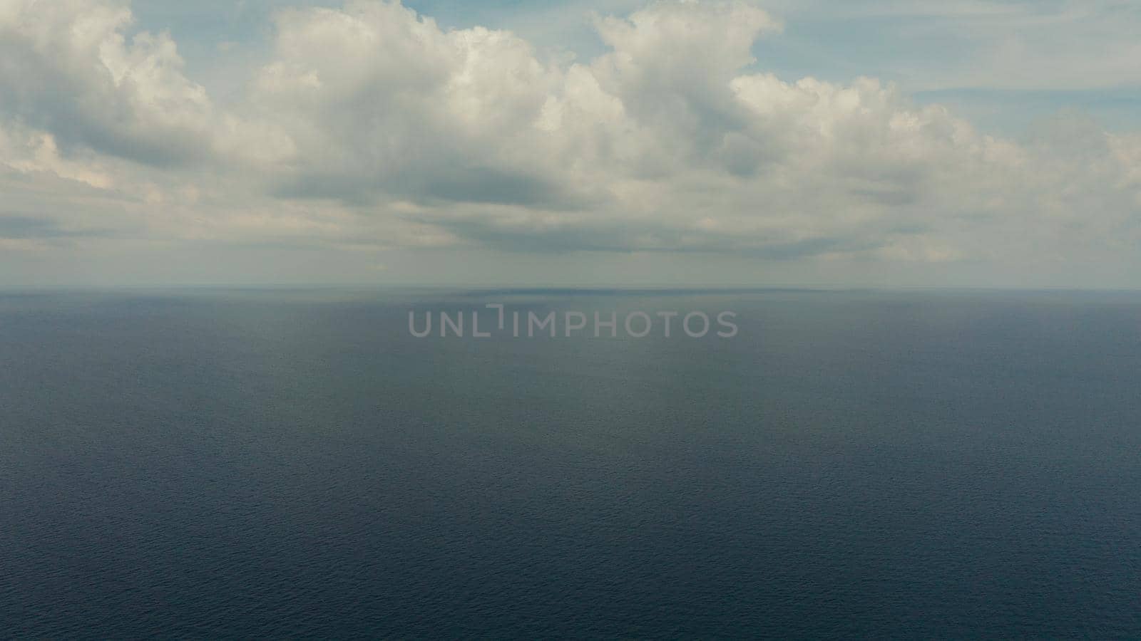 Sea surface with waves against the blue sky with clouds, aerial view. Water cloud horizon background. Blue sea water with small waves against sky.