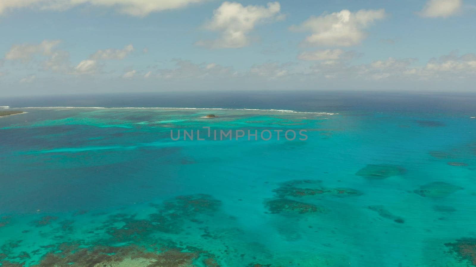 Top view of turquoise water of the atoll against the backdrop of the tropical island and sky with clouds. Travel concept.