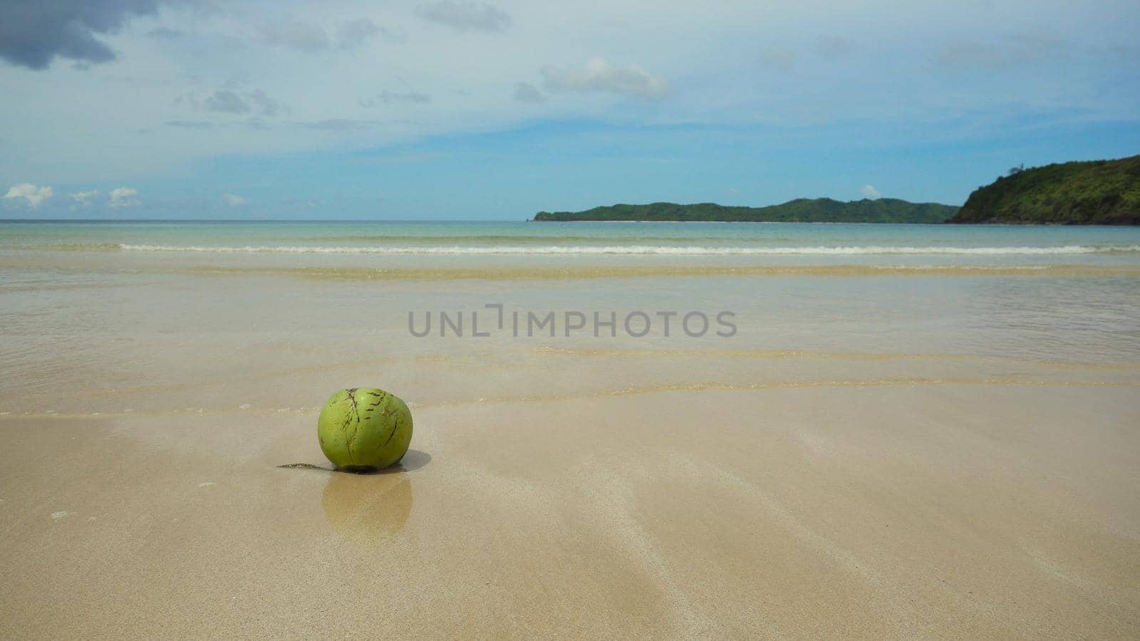 Green coconut on the sand of a tropical beach on a background of blue sky, sea, clouds. Fresh coconut from palm on a sandy beach. Tropical beach, blue sky, clouds.. Philippines El Nido Travel concept.