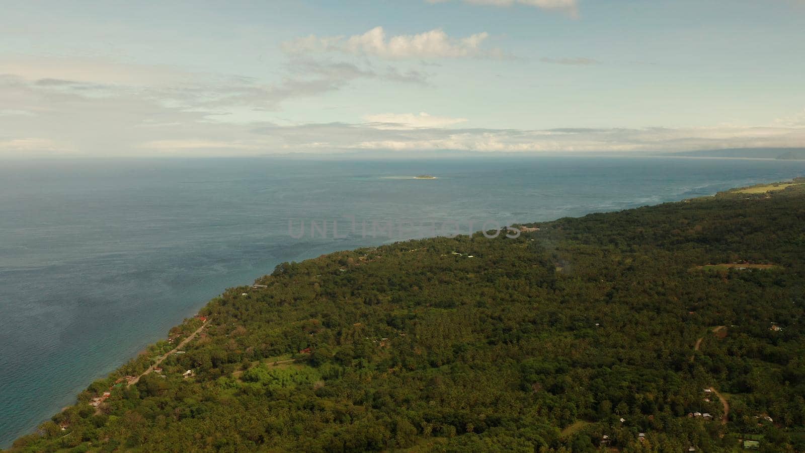 Coastline of tropical island covered with green forest against the blue sky with clouds and blue sea, aerial view. Seascape: Ocean and sky.Philippines, Camiguin.