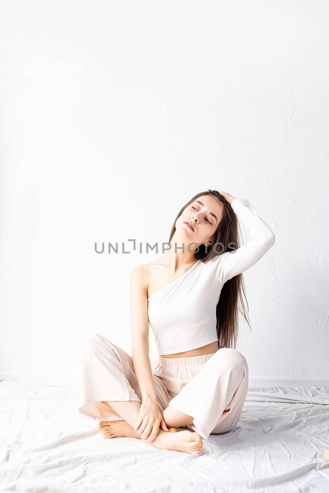 Light and airy. Portrait of beautiful woman in white cozy clothes sitting on the floor looking away