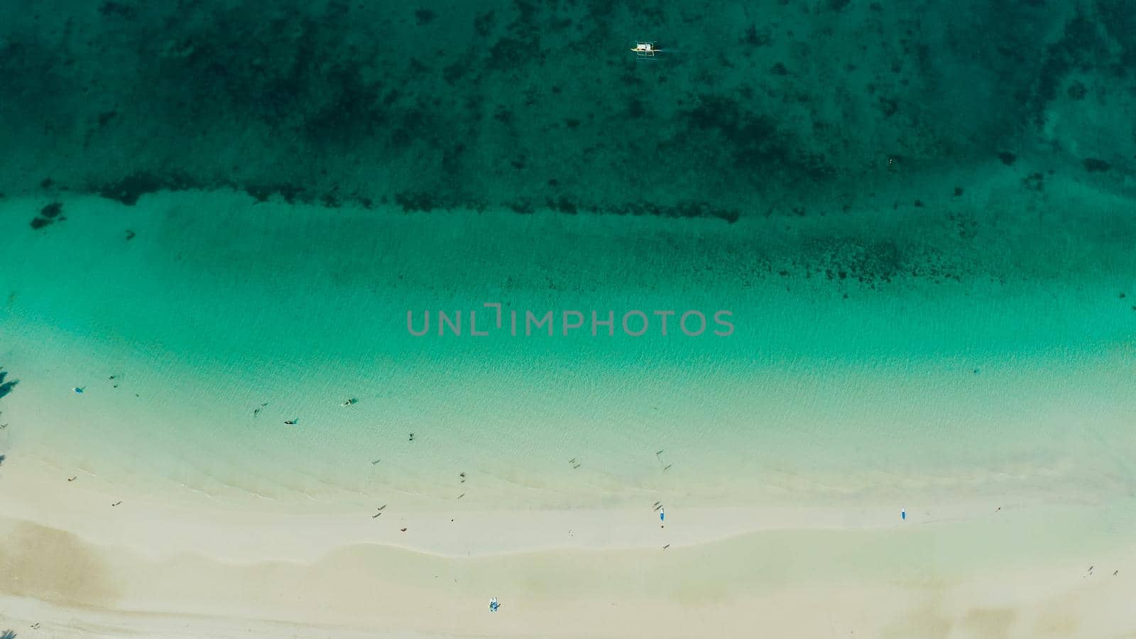 White sandy beach with tourists and azure water of the lagoon,copy space for text, top view. Ocean with waves and tropical beach. Summer and travel vacation concept