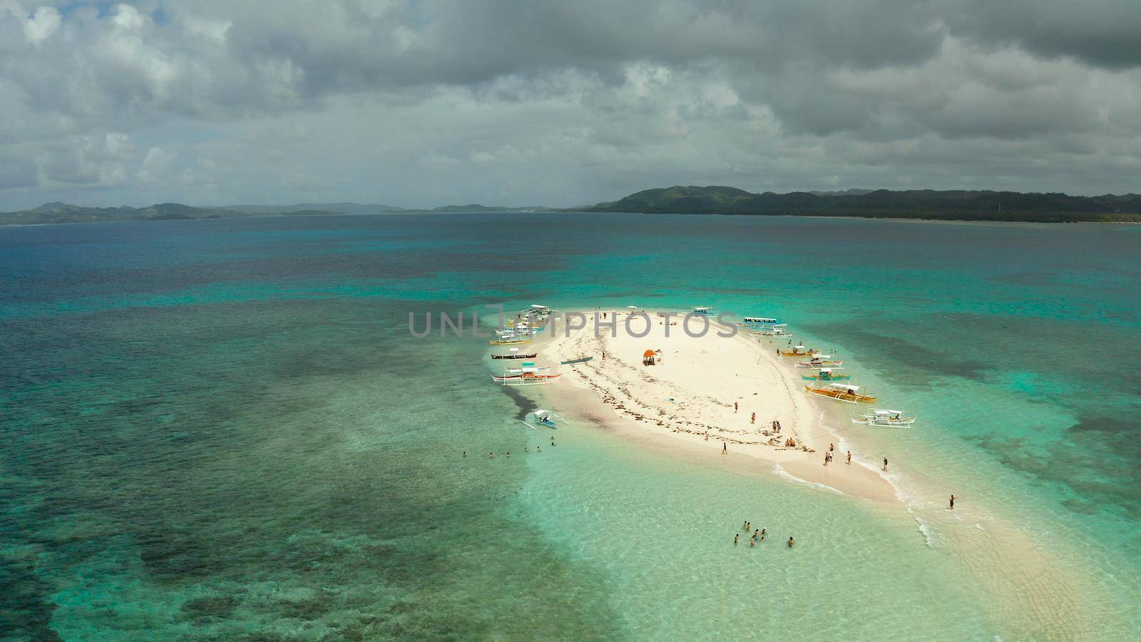 Tropical white island and sandy beach with tourists surrounded by coral reef and blue sea, aerial view. Naked Island, Siargao Summer and travel vacation concept