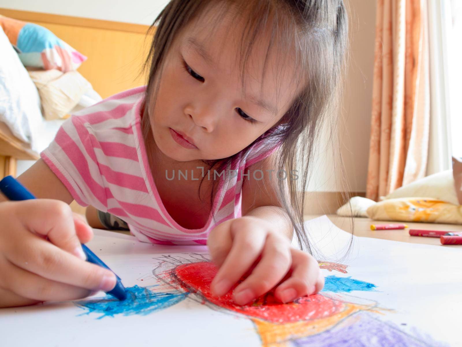 Asian girl Painting crayon on large sheets of paper On the floor of her room