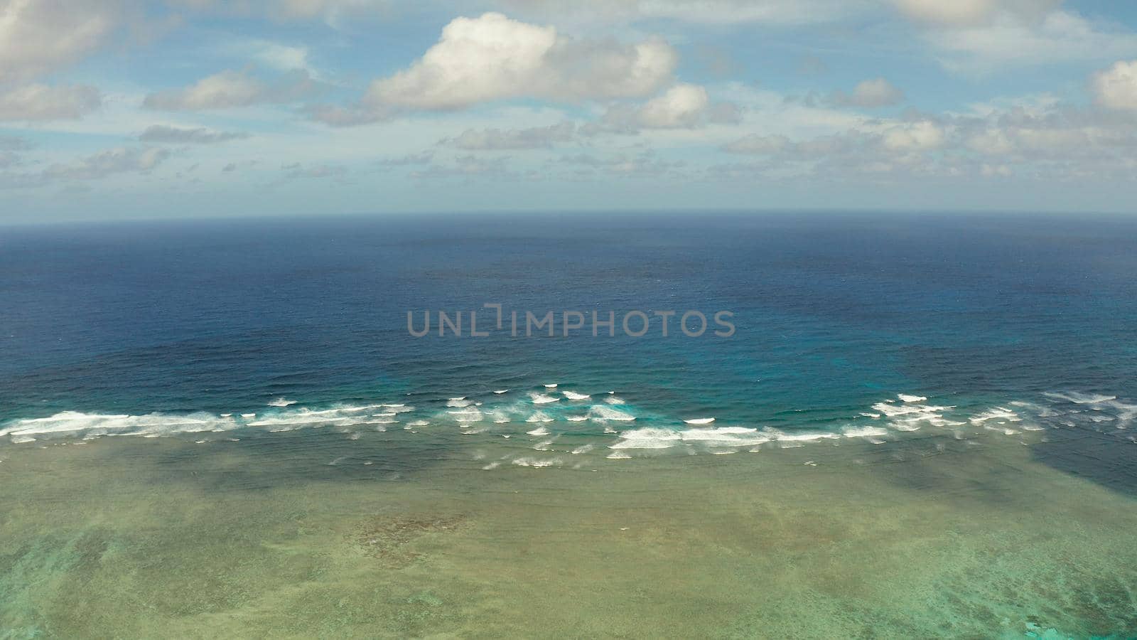 Sea surface with waves against the blue sky with clouds, top view. Blue sea water with waves against sky. Siargao, Philippines.