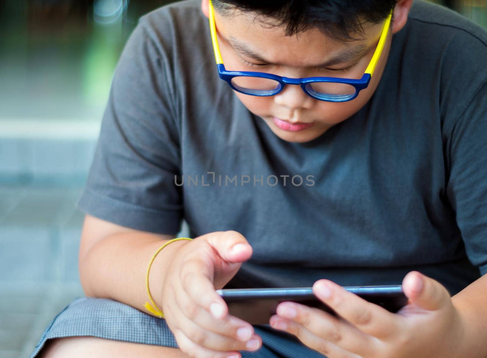 Asian boy have a serious face while playing game on smartphone by Satakorn
