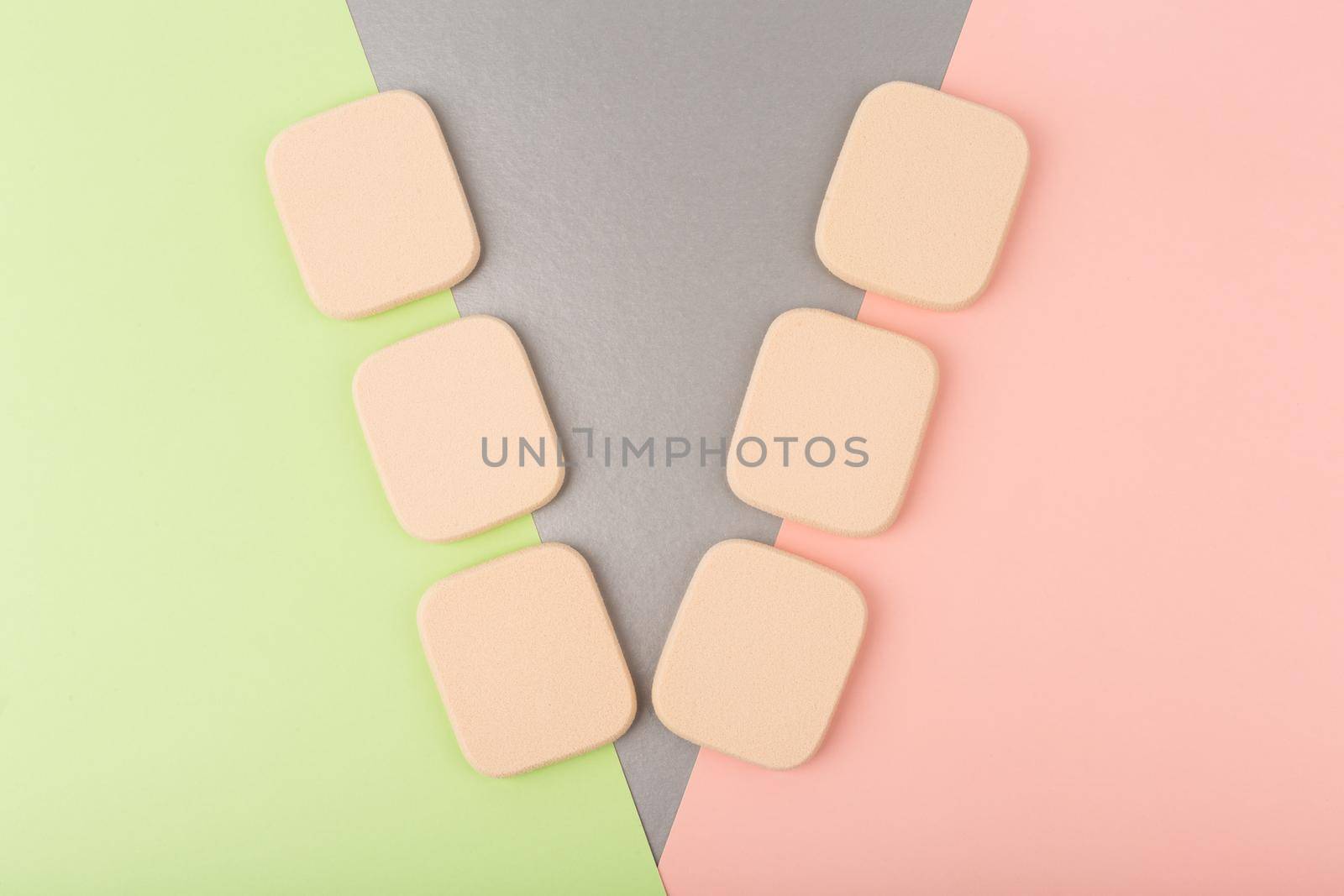 Minimalistic flat lay with with two rows of square shaped make up sponges against colored pink, silver and green background. High quality photo