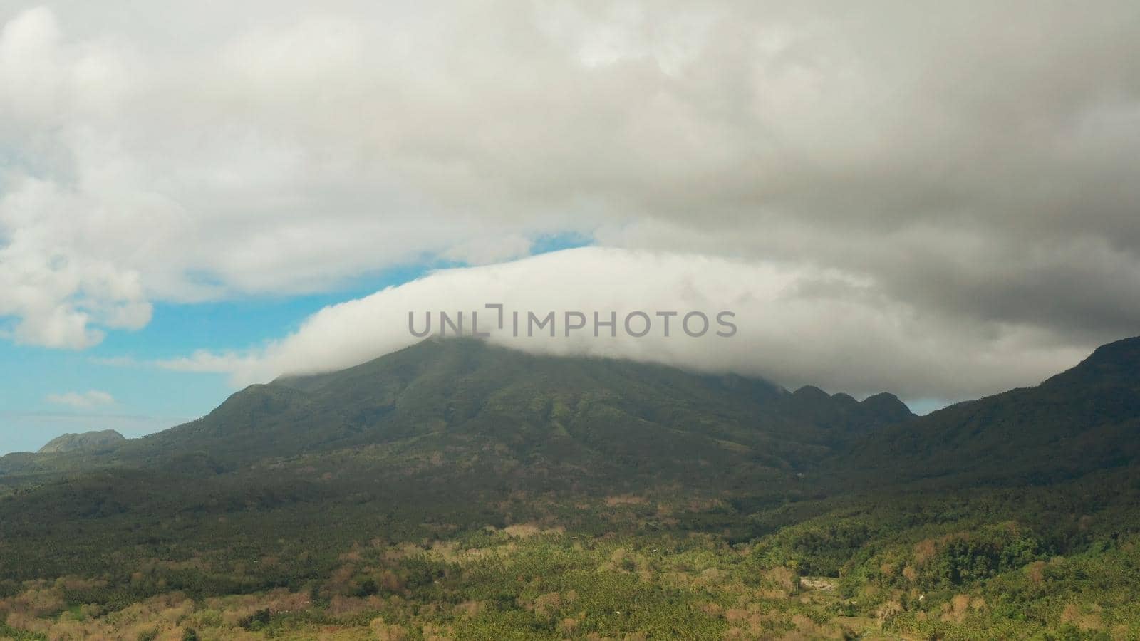 Aerial view of mountains covered rainforest, trees. Camiguin, Philippines. Mountain landscape on tropical island with mountain peaks covered with forest. Slopes of mountains with evergreen vegetation.