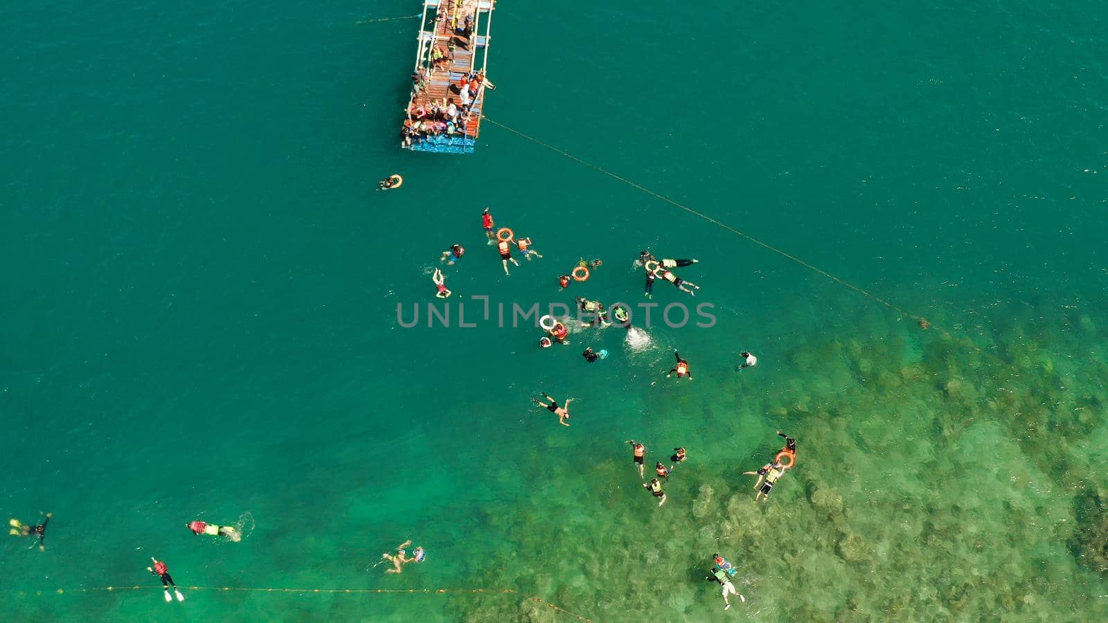 Tourists snorkeling over coral reef with clear blue ocean water, aerial view. People swim in the transparent sea between coral reefs. Summer and travel vacation concept.