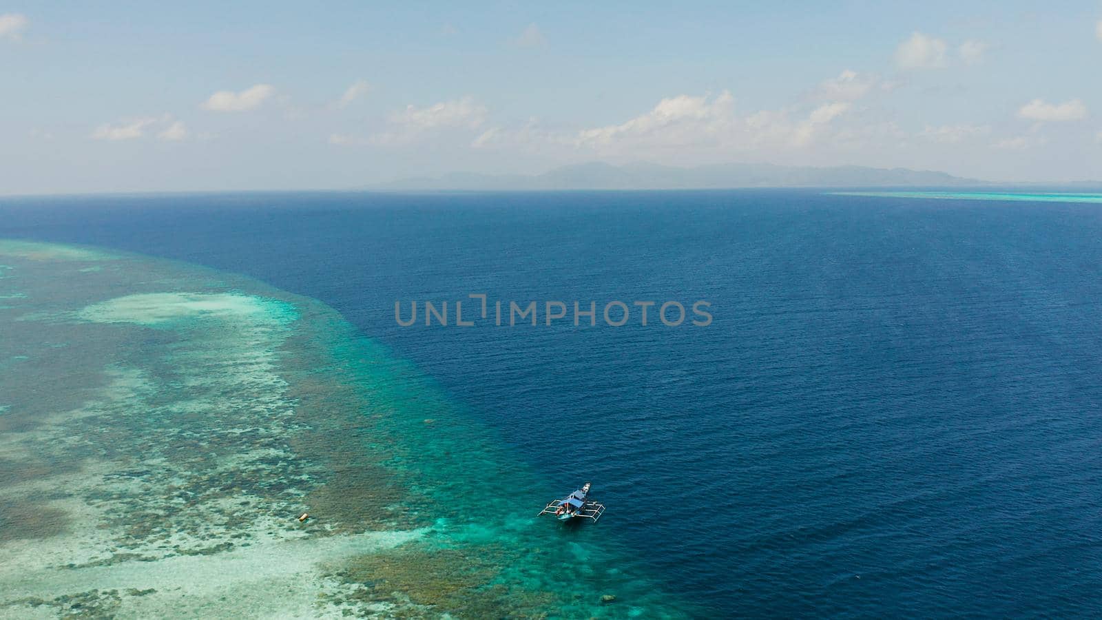 Boat with tourists stopped on a coral reef for snorkeling from above. Summer and travel vacation concept. Balabac, Palawan, Philippines.