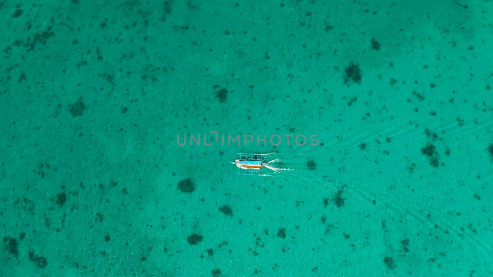 Tourist motor boat on the surface of turquoise water in tropical lagoon, aerial view. Seascape with beach on tropical island. Summer and travel vacation concept. Boracay Island, Philippines
