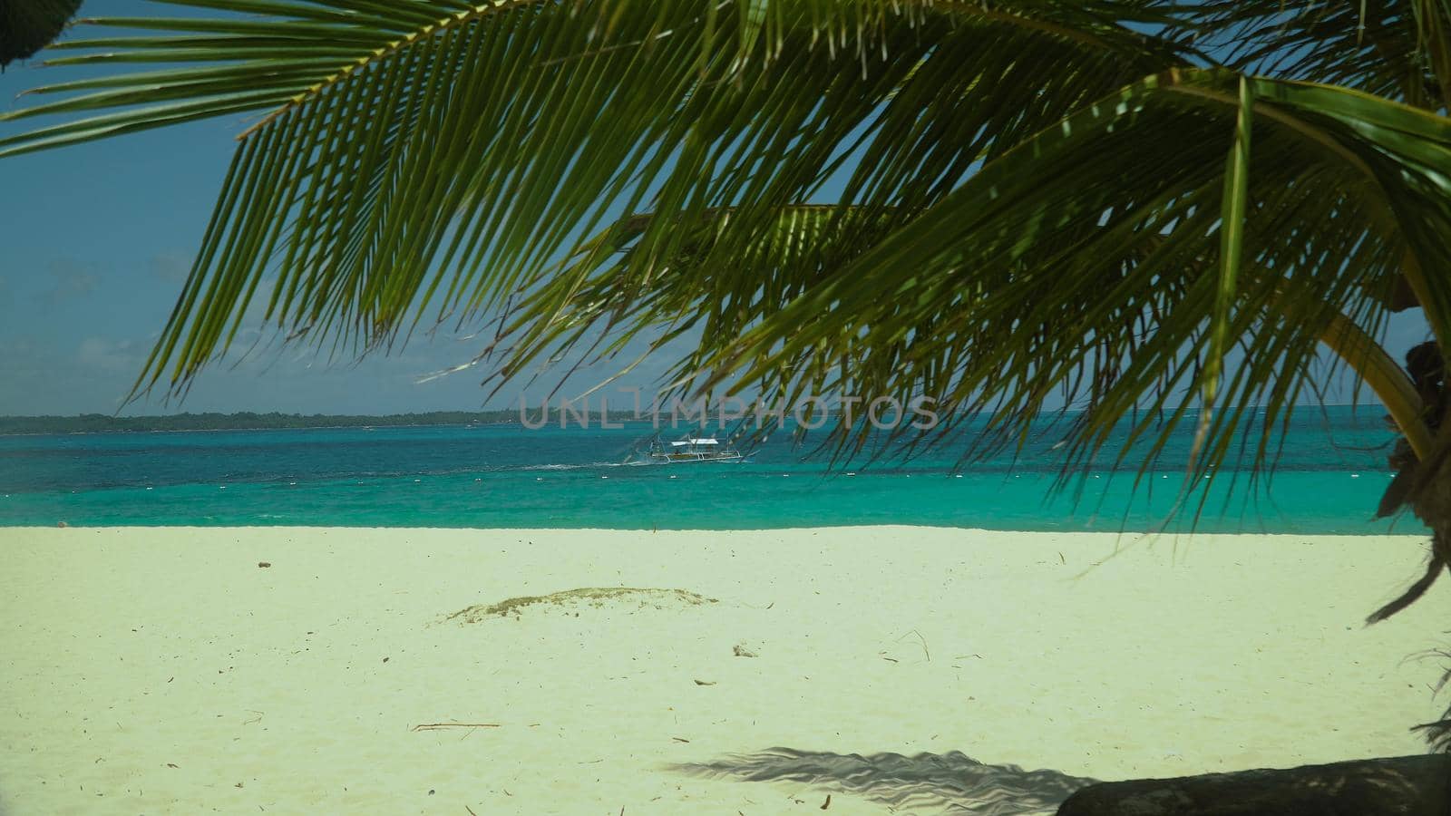 Tropical sandy beach and blue sea through palm branches. Summer and travel vacation concept. Boracay, Philippines