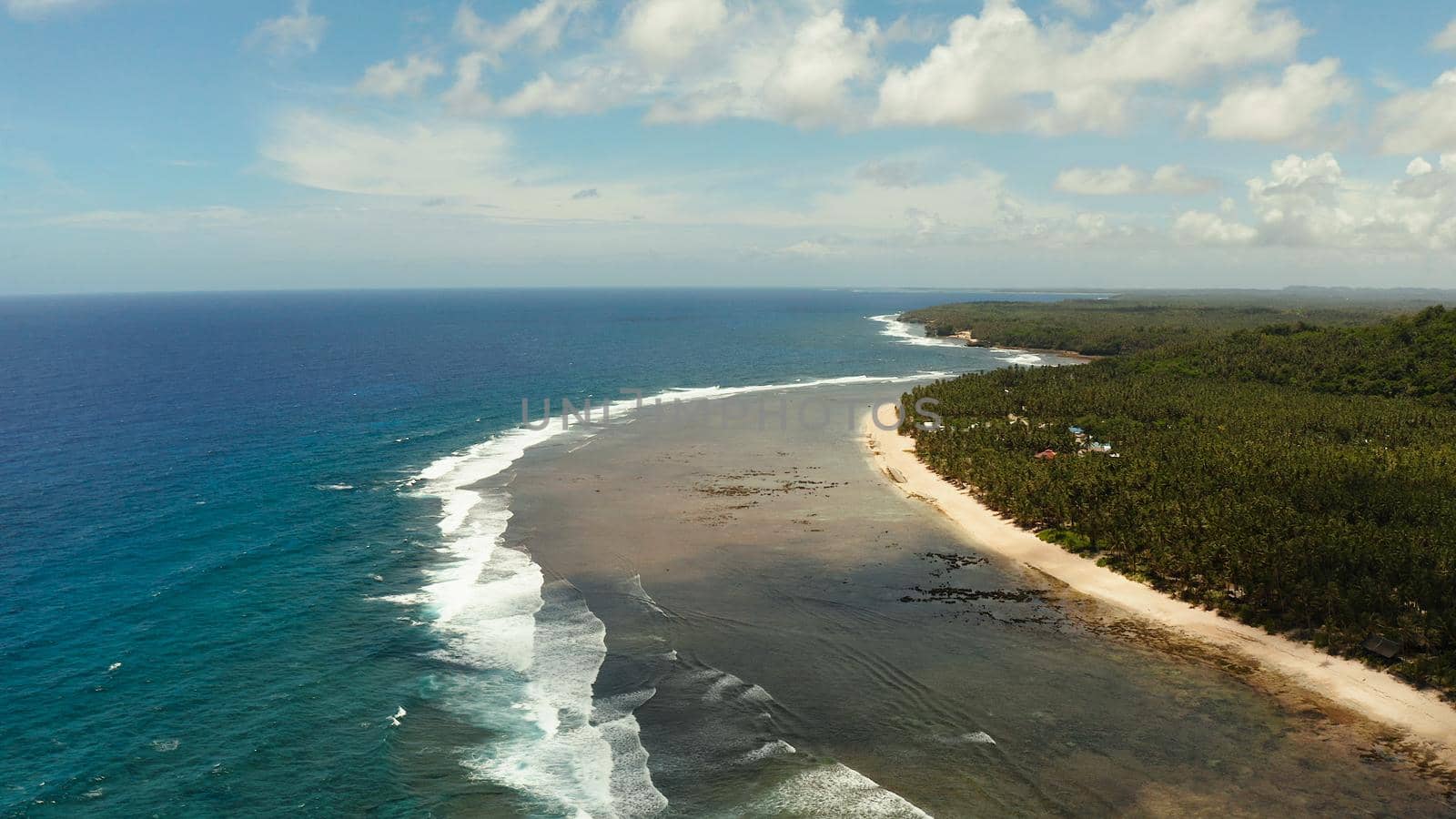 Seascape with the coast of the tropical island covered with forest and palm trees against the sky and blue water. Siargao,Philippines