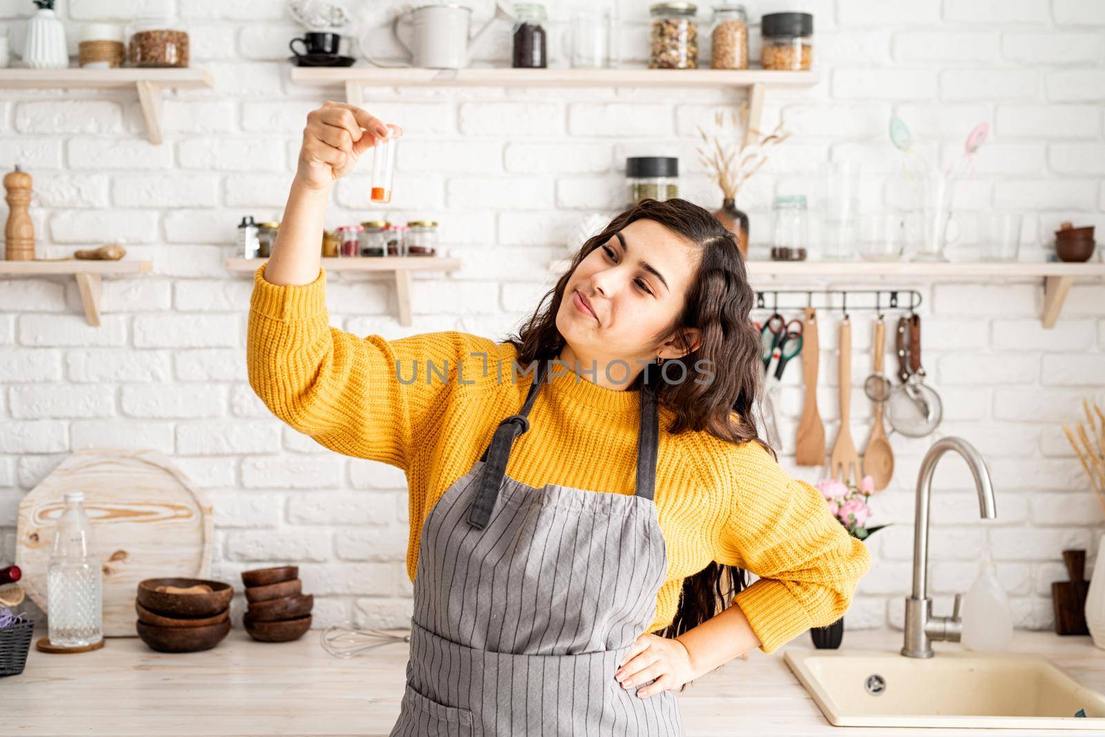 Beautiful brunette woman in yellow sweater and gray apron coloring easter eggs in the kitchen holding test tube with orange color