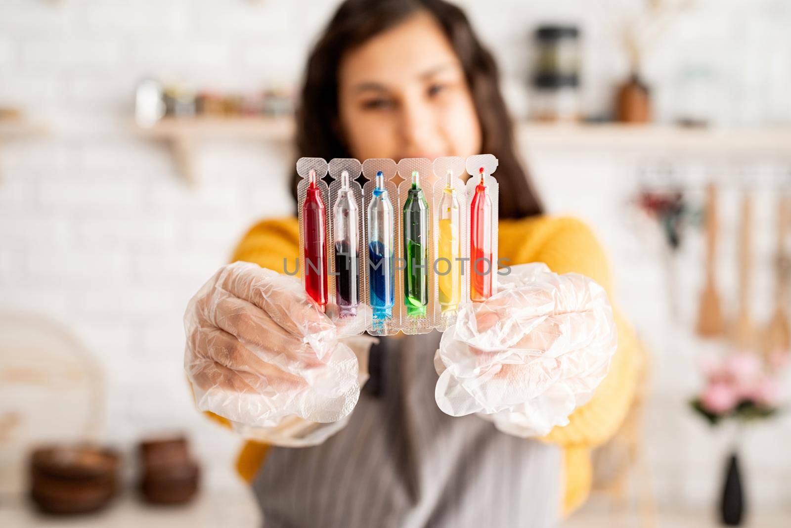 Beautiful woman coloring easter eggs in the kitchen holding tubes with colorful liquids