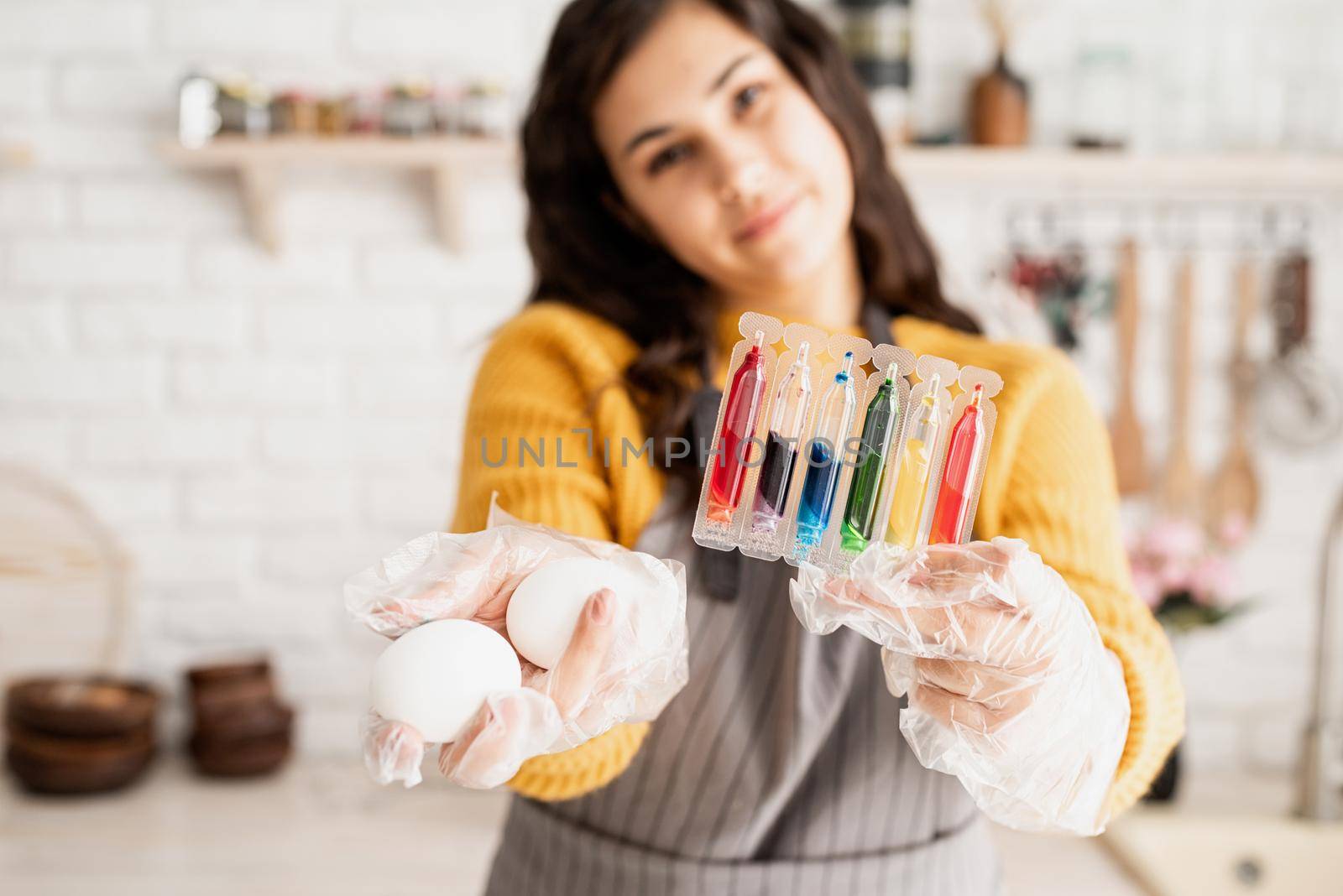 Beautiful woman coloring easter eggs in the kitchen holding tubes with colorful liquids and white eggs