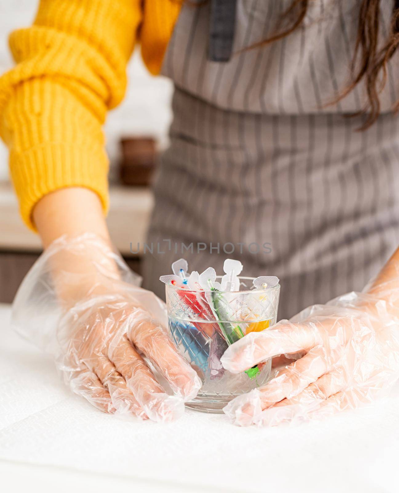 Beautiful brunette woman in yellow sweater and gray apron preparing to color easter eggs in the kitchen