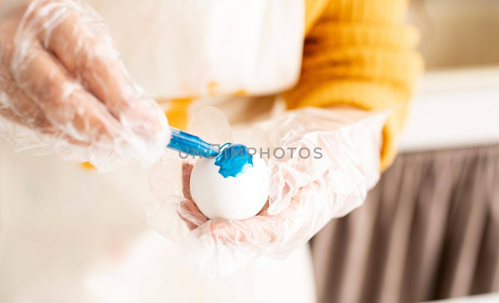 Close up of woman hands in gloves coloring easter eggs blue