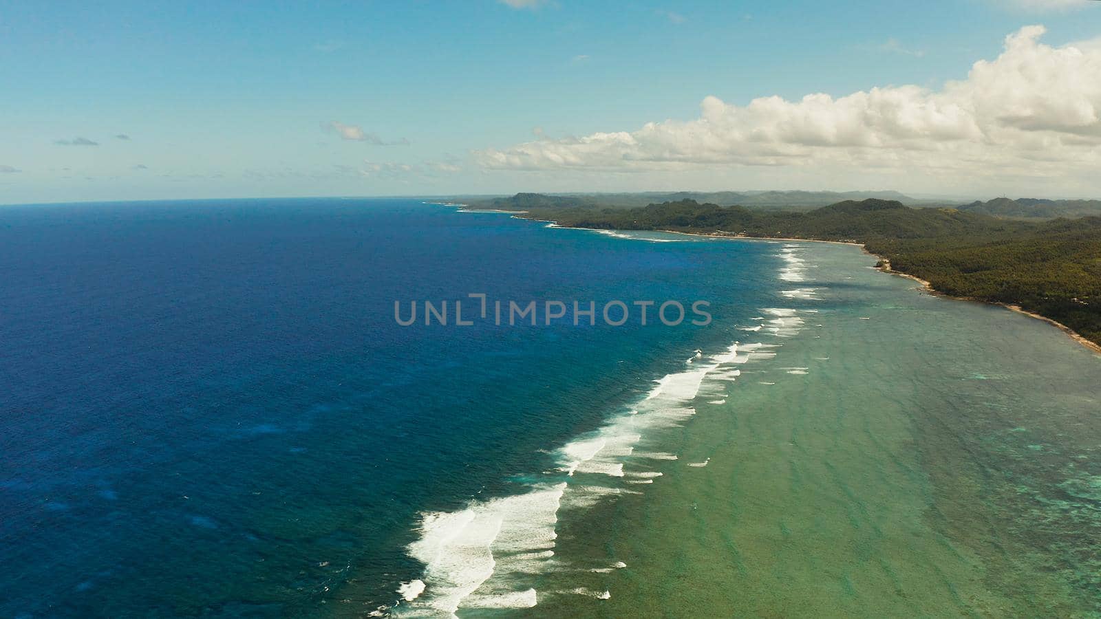 Seascape with the coast of the tropical island covered with forest and palm trees against the sky and blue water. Siargao,Philippines