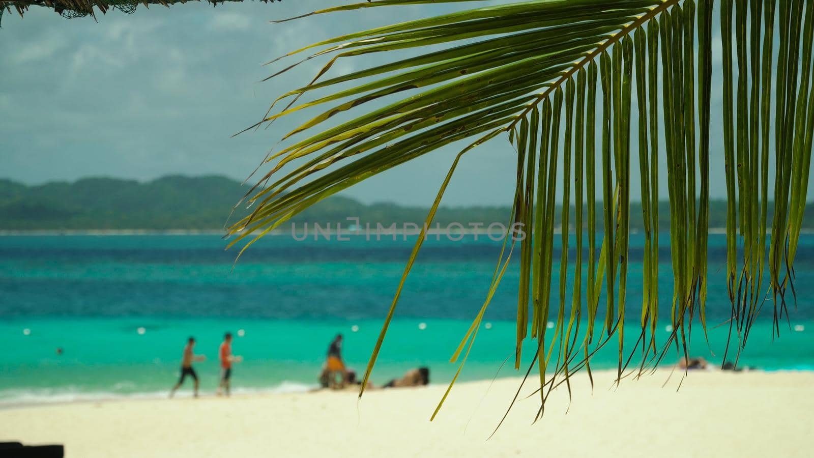 Tropical beach with tourists and clear blue sea through palm branches. Summer and travel vacation concept. Philippines