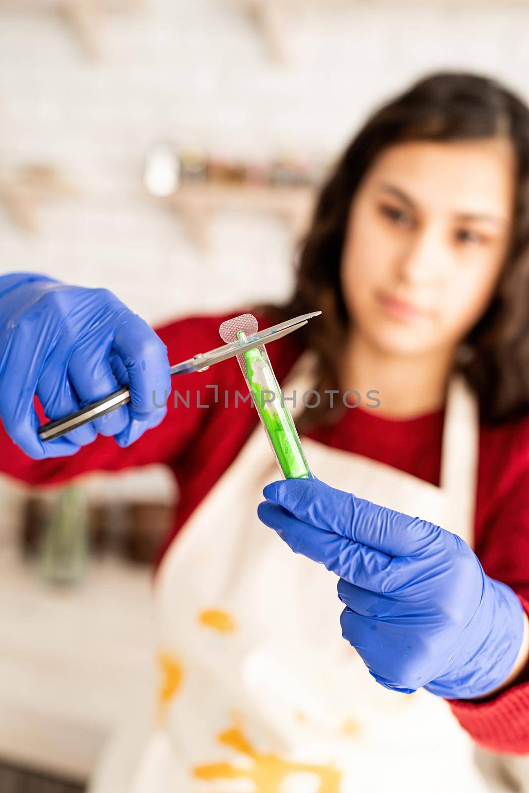 Beautiful brunette woman in red sweater and white apron coloring easter eggs in the kitchen opening tube with color liquid