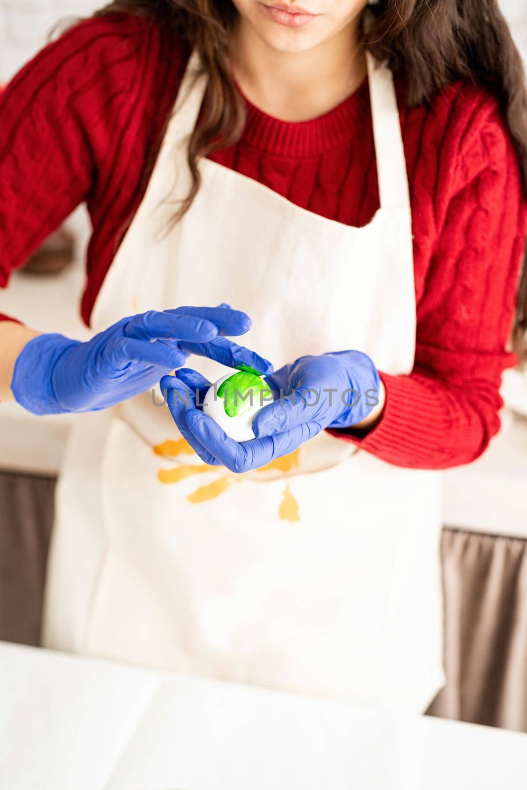 Beautiful brunette woman in red sweater and white apron coloring easter eggs in the kitchen