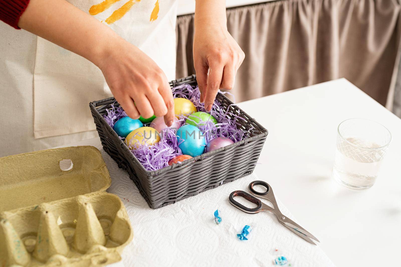 Beautiful smiling brunette woman in red sweater and white apron decorating colorful easter eggs