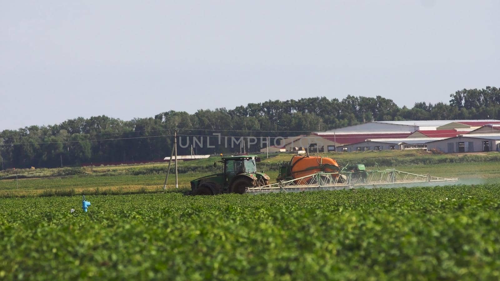 Aerial view tractor spraying the chemicals on the large green field. Spraying the herbicides on the farm land. Treatment of crops against weeds.