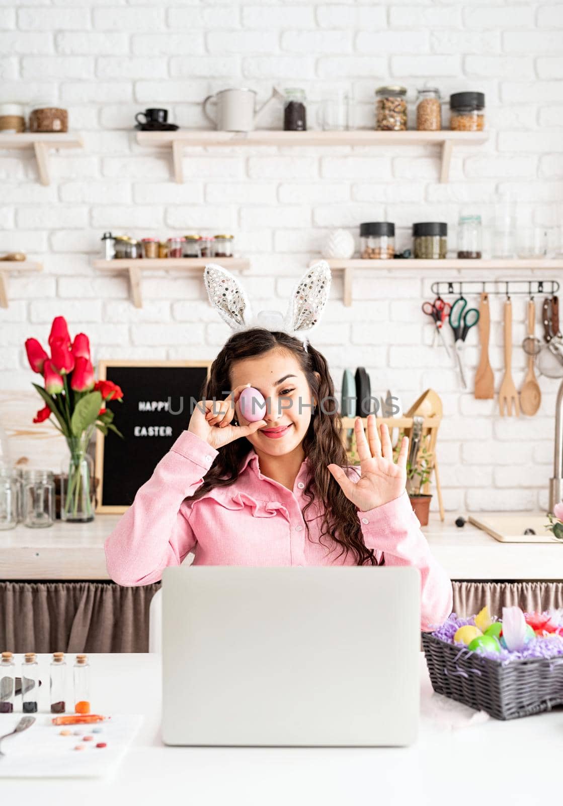 Funny woman greeting her friends online, celebrating easter, covering her eyes with colorful eggs