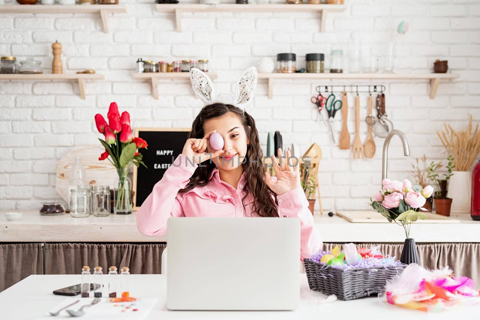 Funny woman greeting her friends online, celebrating easter, covering her eyes with colorful eggs