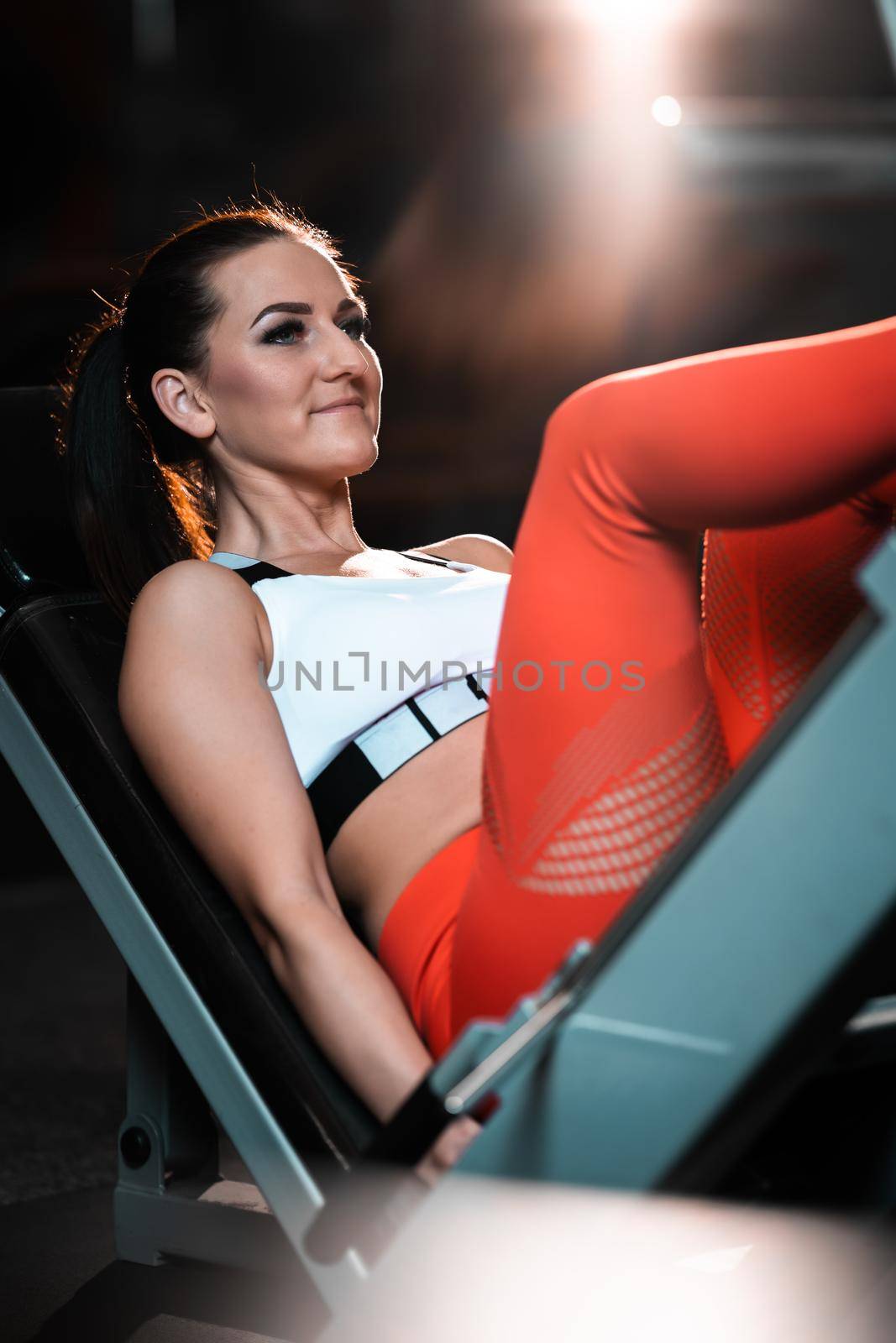 Young woman practicing legs on the machine in a gym by Edophoto