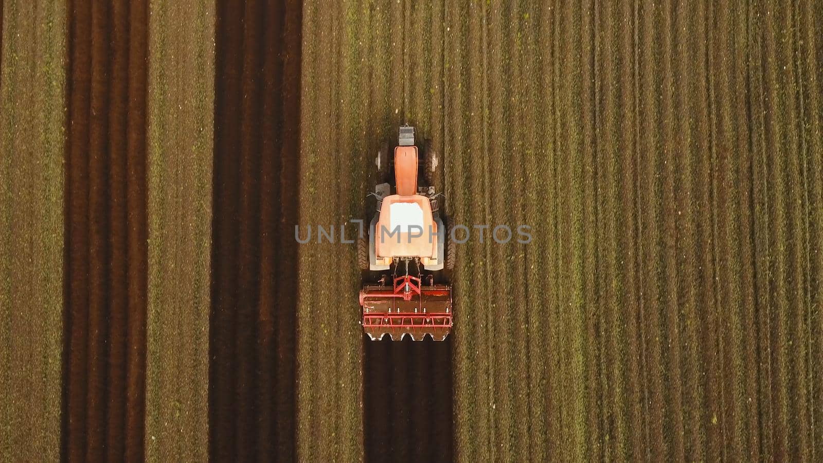Farmer in tractor preparing land with seedbed cultivator in farmlands. Tractor plows a field. Agricultural work in processing, cultivation of land. Farmers preparing land and fertilizing. Agricultural workers with tractors.