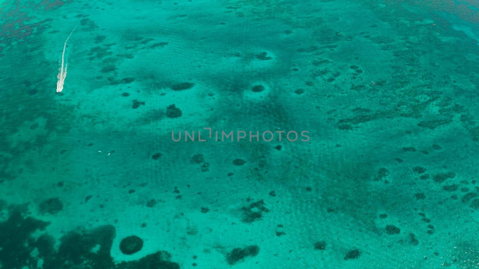 Tourist motor boat on the surface of turquoise water in tropical lagoon, aerial view. Seascape with beach on tropical island. Summer and travel vacation concept. Boracay Island, Philippines