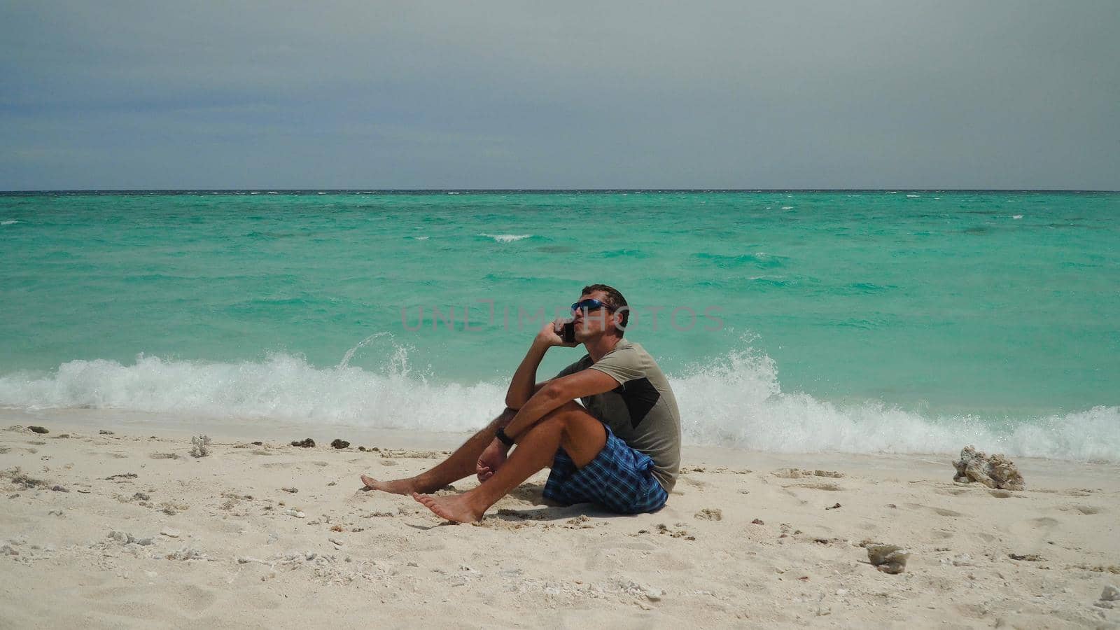 A man sits and talks on a cell phone on a tropical beach. Summer and travel vacation concept.