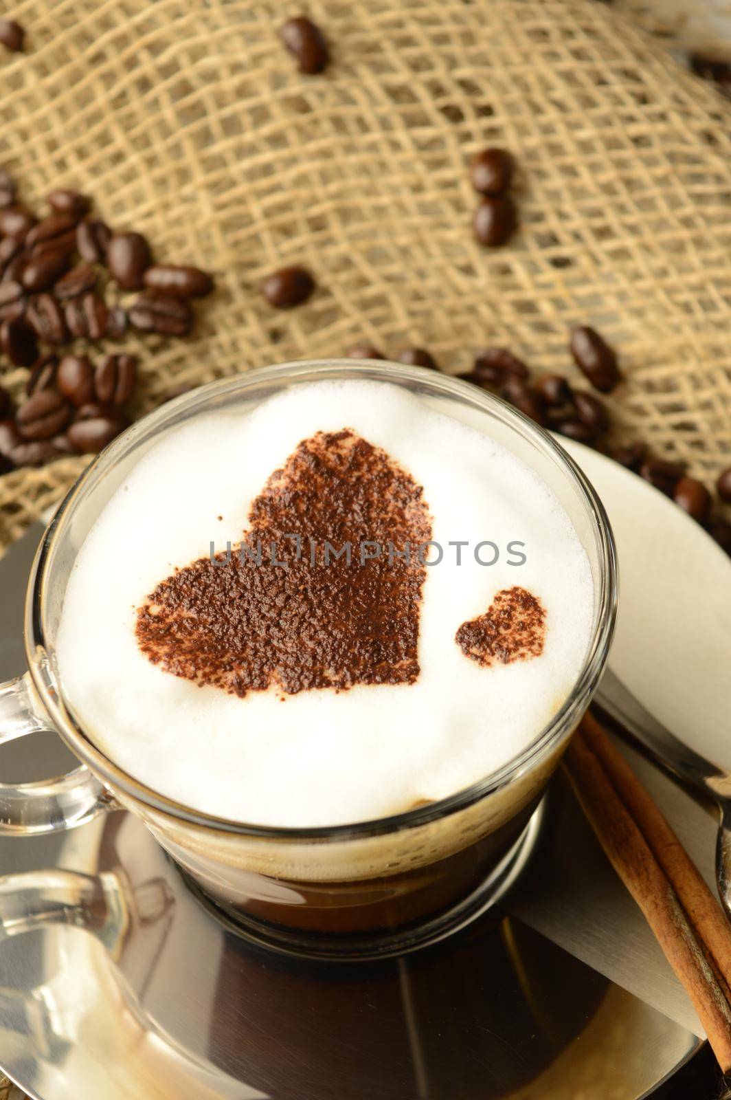 A specialty cup of brewed coffee with a heart shape design while resting among roasted beans.